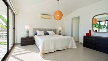 A modern bedroom with a large bed, bedside lamps, a hanging light fixture, a mirror, and a dresser.