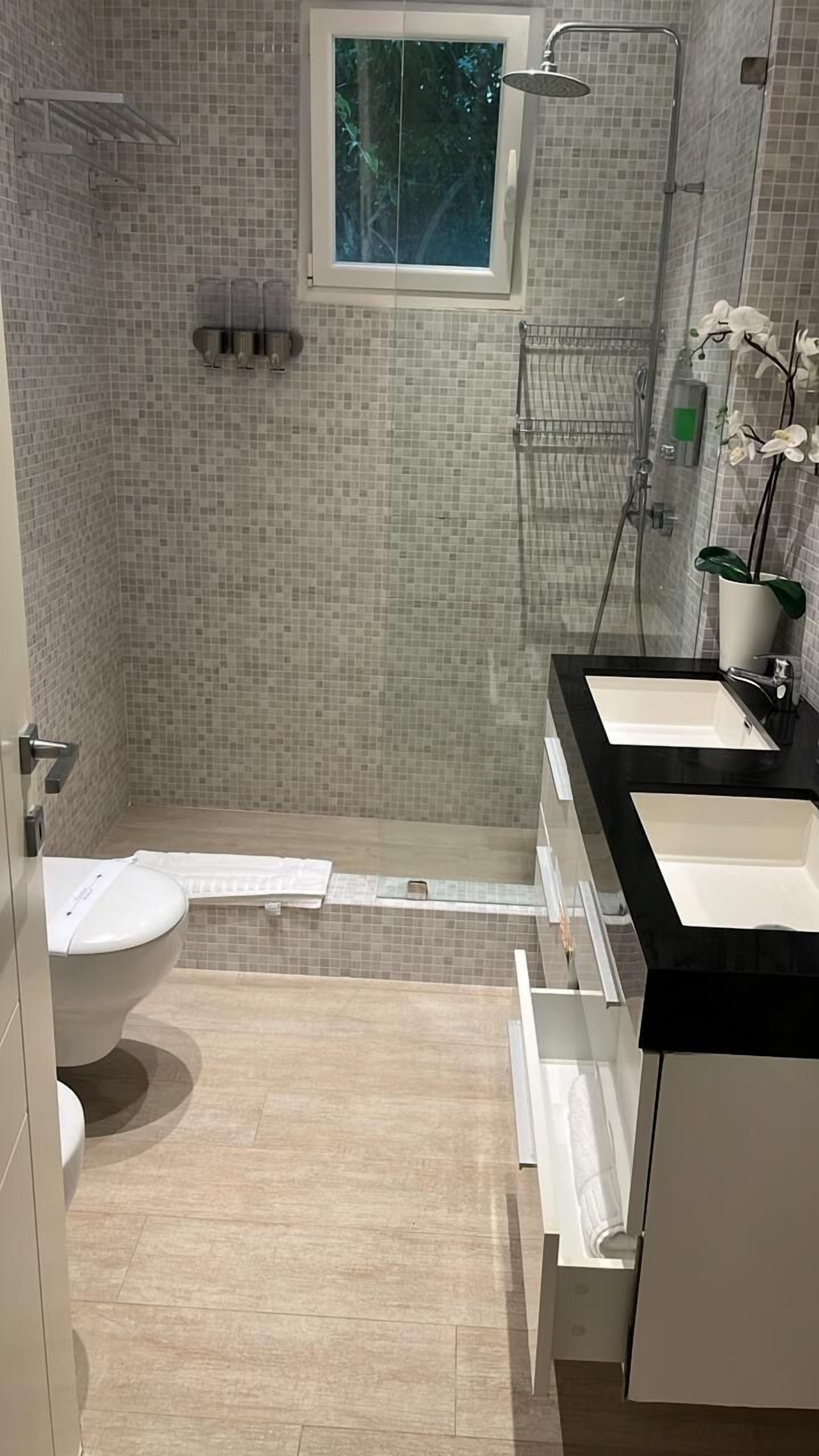 Ein Badezimmer mit Dusche, zwei Waschbecken, Toilette und einem Fenster.