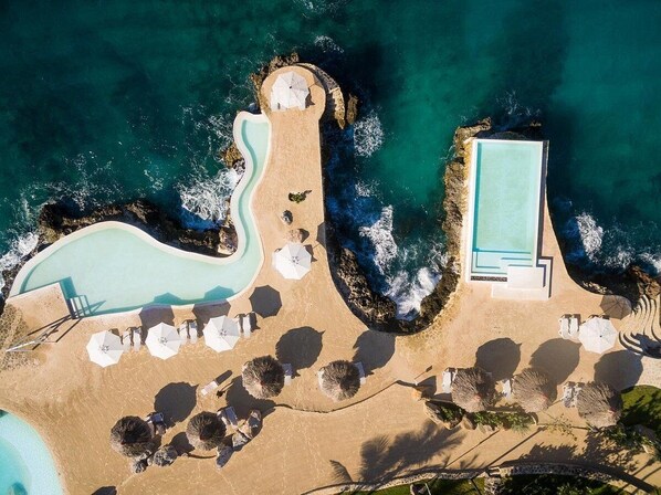 An aerial view of a resort with a large swimming pool, a separate pool, and a beach area with umbrellas and lounge chairs. - TRACADERO Beach Club and Holidays Rentals (San Rafael del Yuma)
