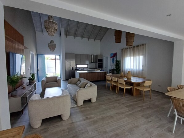 A spacious living area with a large sofa set, a dining table with chairs, and a kitchen in the background.