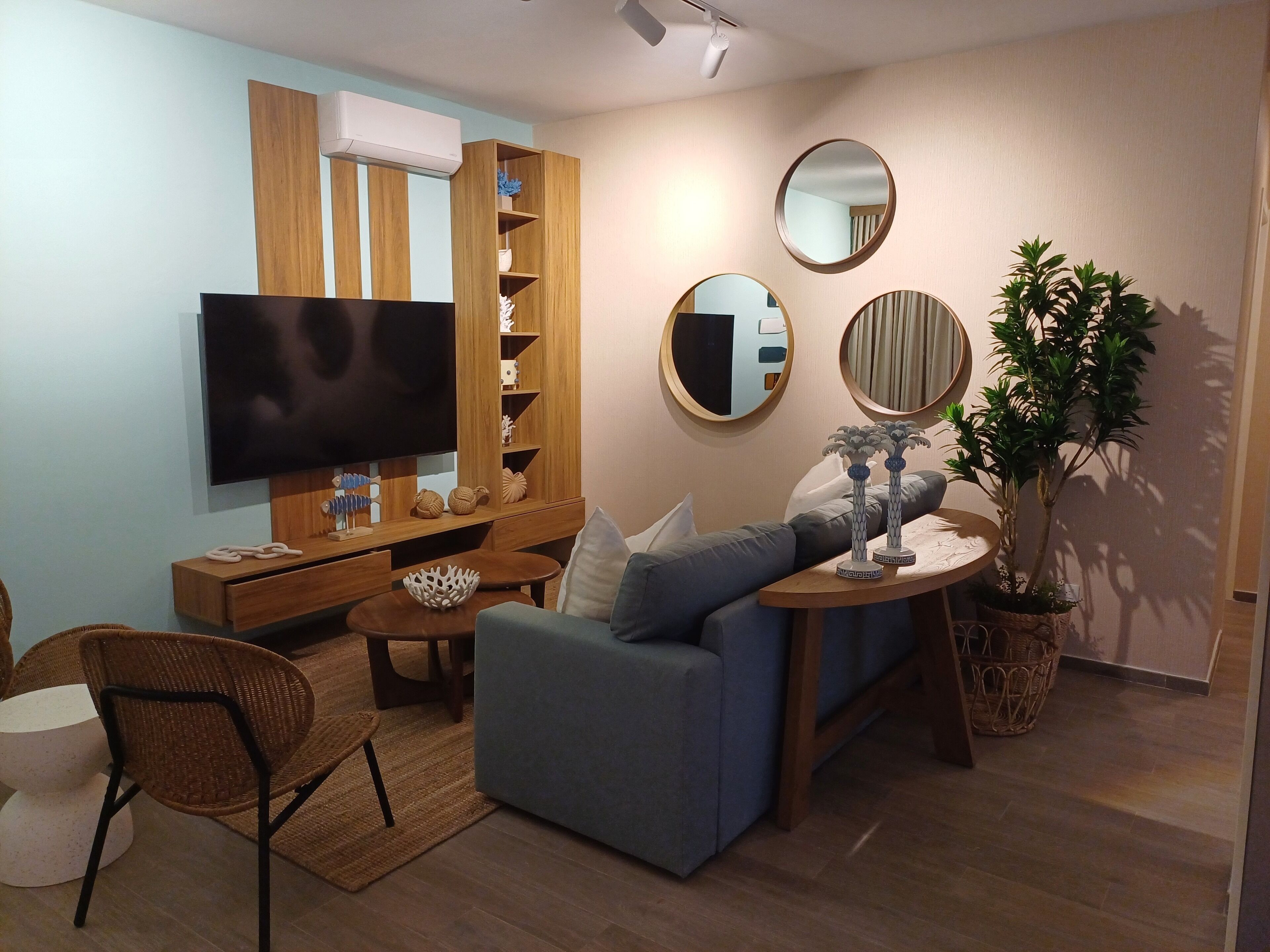 Una sala de estar moderna con una televisión de pantalla plana, un sofá azul, un mueble de entretenimiento de madera y una planta en maceta.