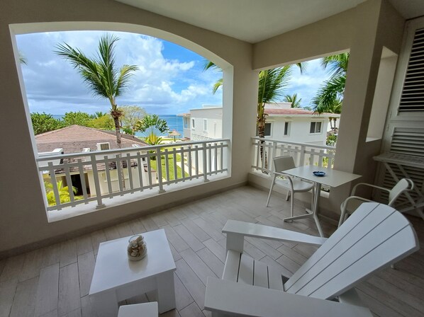 A balcony with white furniture, a table with a decorative item, and a view of the sea and buildings. - TRACADERO Beach Club and Holidays Rentals (San Rafael del Yuma)