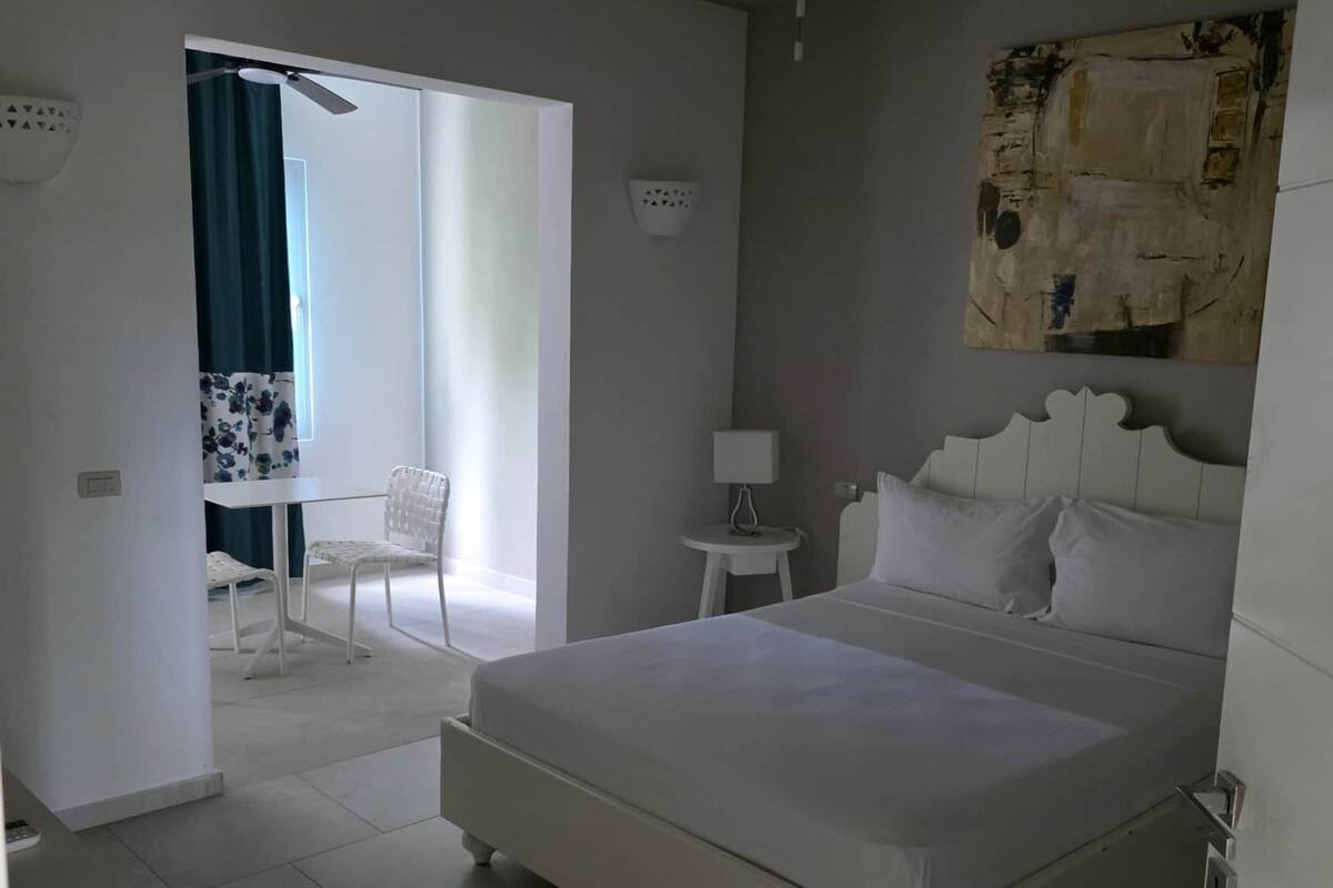 A bedroom with a large bed, a ceiling fan, a small table with a lamp, and a chair.