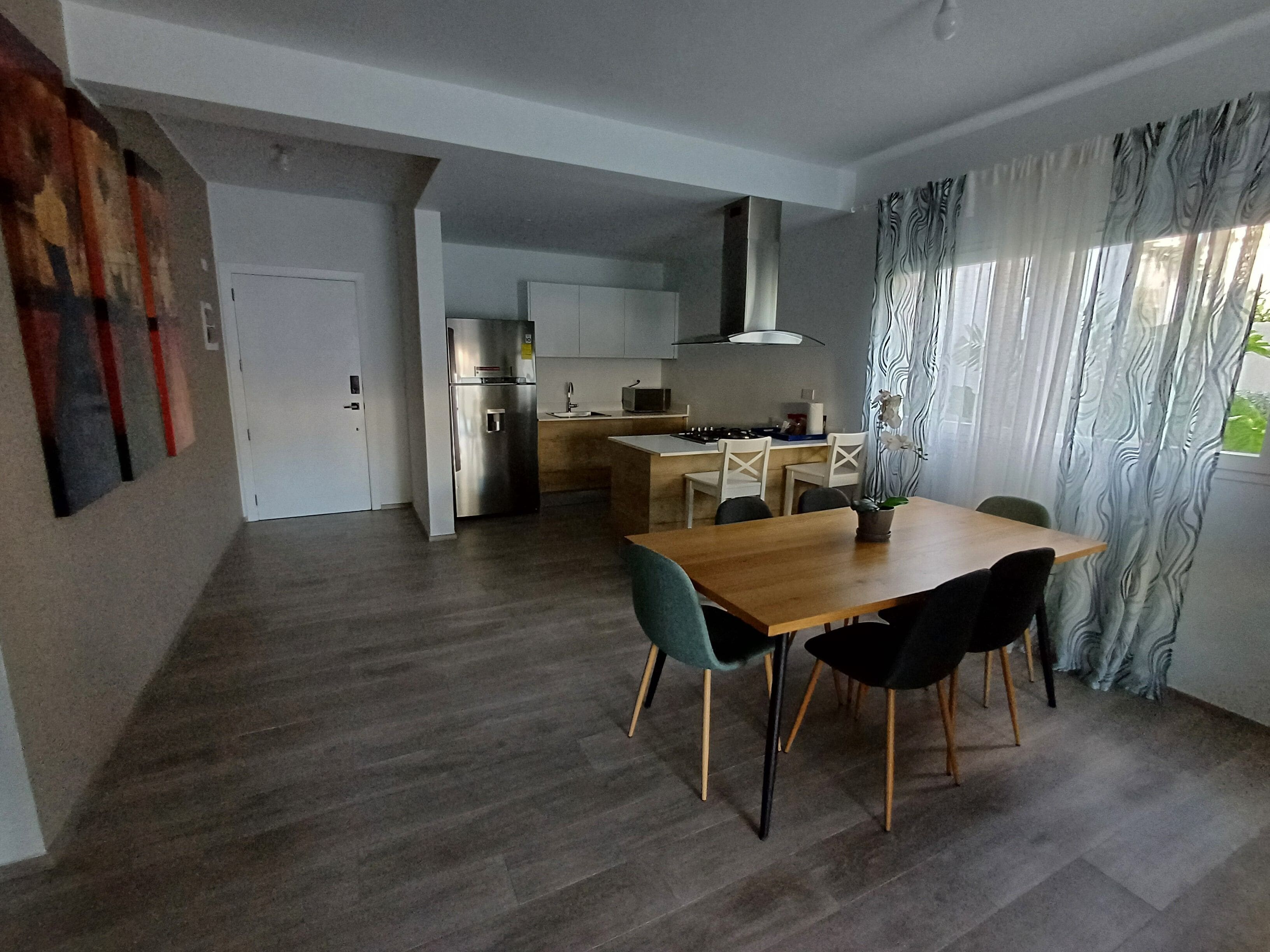 A modern kitchen with a built-in oven, a refrigerator, and a dining area with a wooden table and chairs.