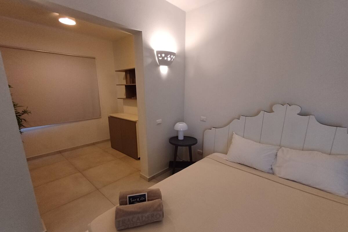 A bedroom with a bed, a nightstand, a wall-mounted lamp, and a small table with a lamp.