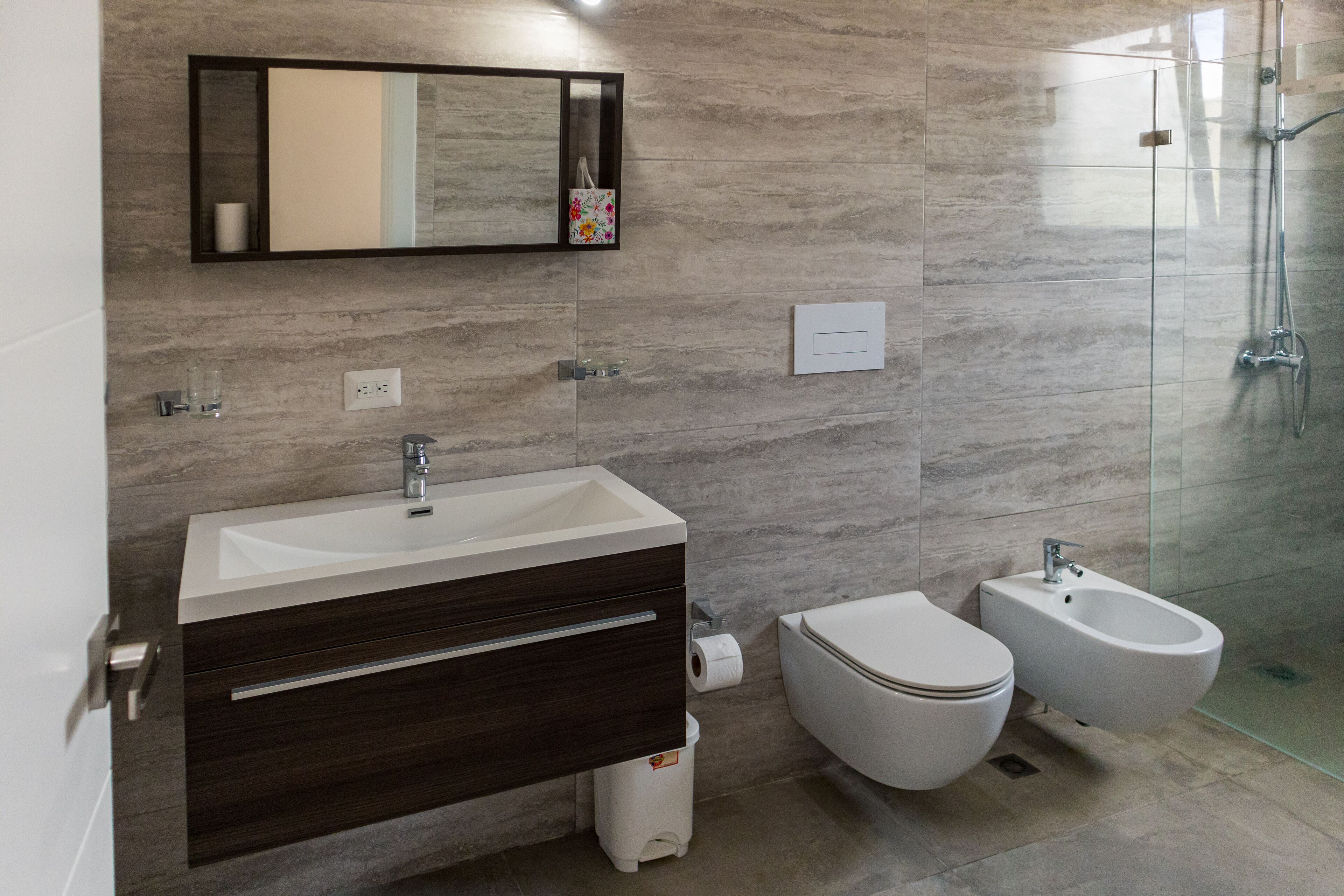A modern bathroom with a sink, mirror, toilet, bidet, and glass shower enclosure.