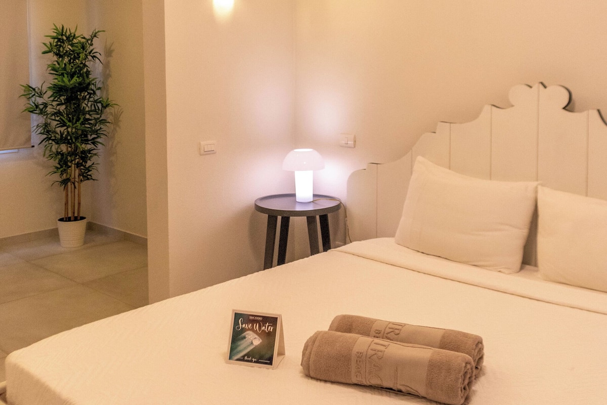 A neatly made bed with a pillow, a bedside lamp, and a book on the nightstand.