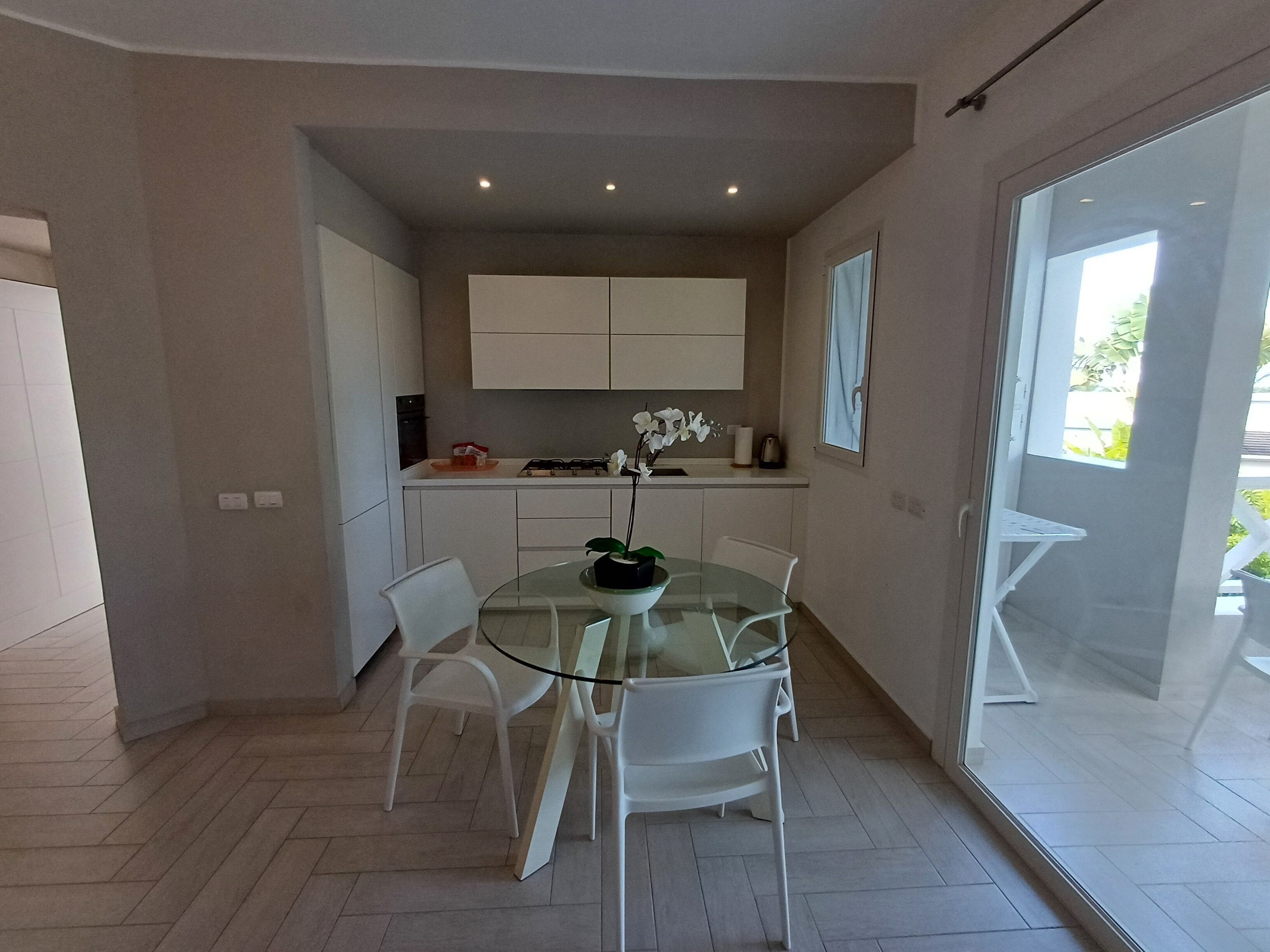 A modern kitchen with white cabinets, a glass dining table, and white chairs.