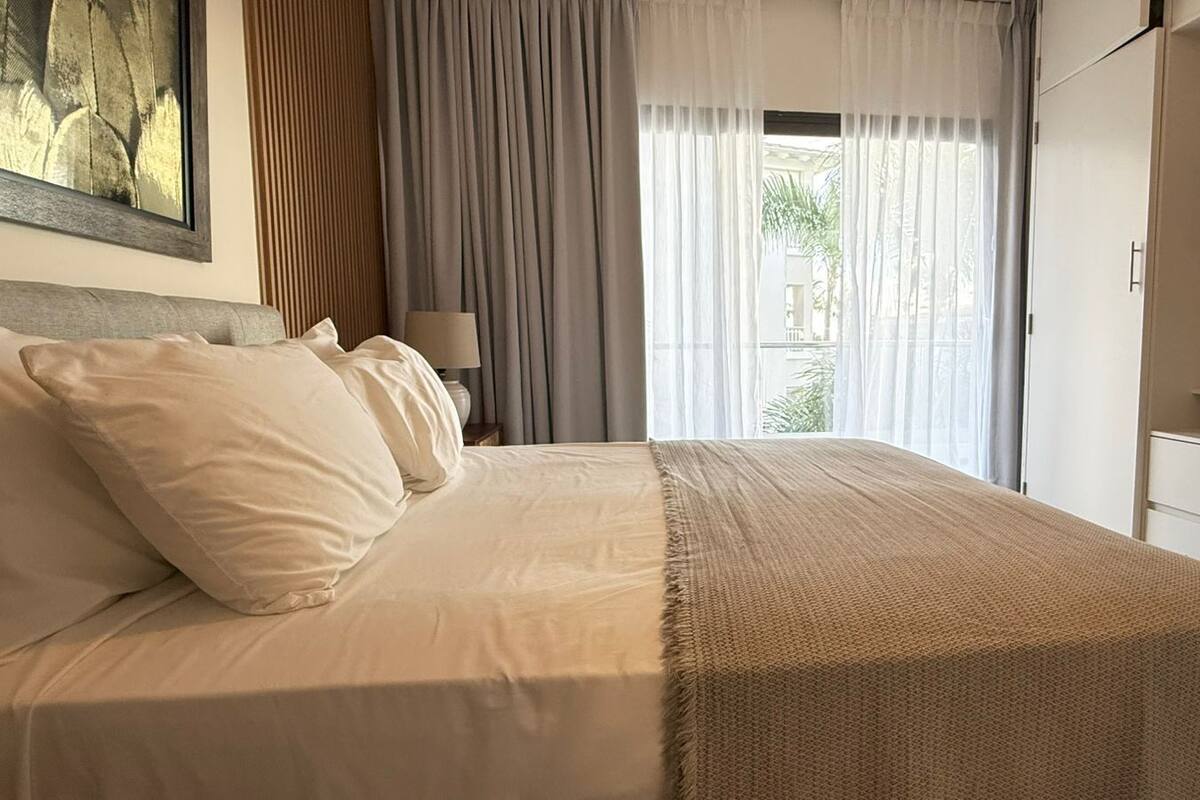 A bedroom with a bed, curtains, a TV, and a view of the outdoors.