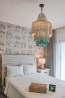 Habitación de hotel con cama, mesita de noche, lámpara, un candelabro decorativo y papel tapiz floral.