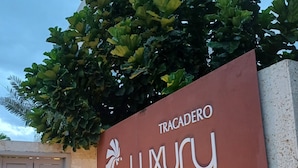 A sign for 'TRACADERO LUXURY' with a logo, set against a wall with a small garden area and a gate. - TRACADERO Beach Club and Holidays Rentals (San Rafael del Yuma)