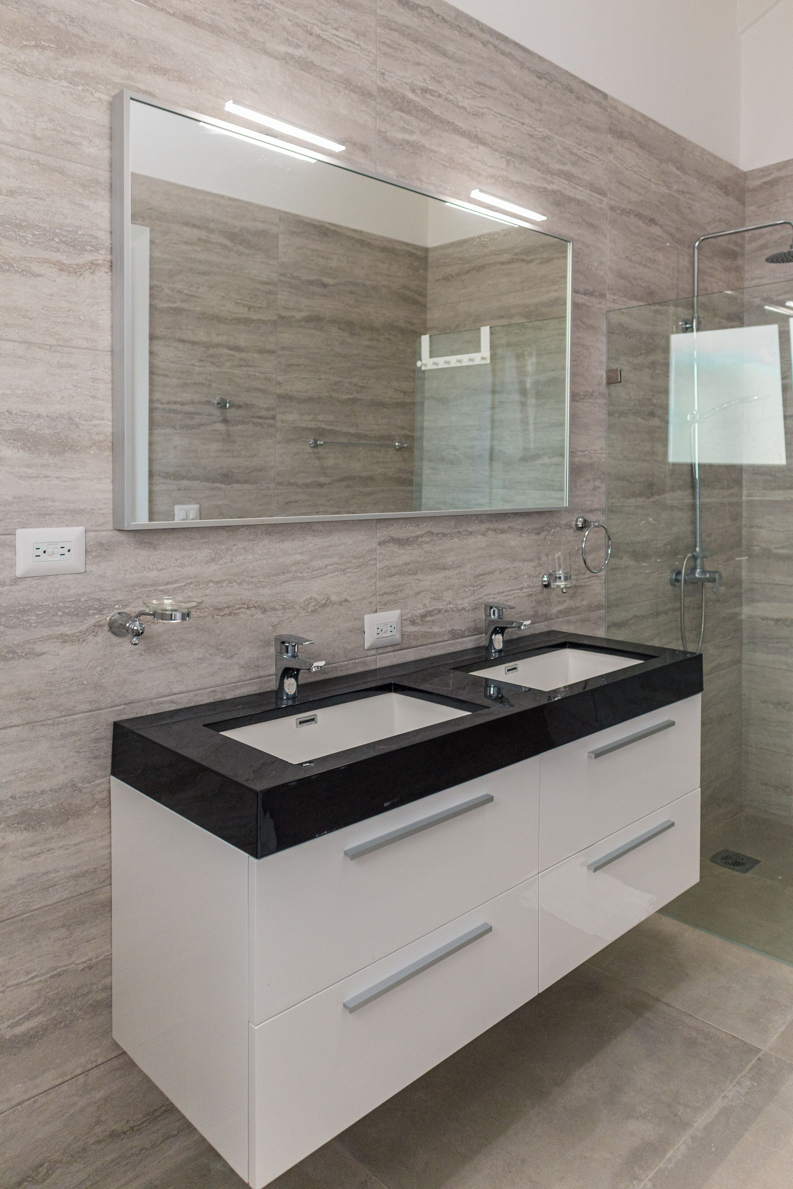A modern bathroom with two sinks, a large mirror, and a glass-enclosed shower.