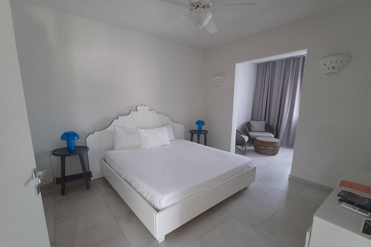 A modern hotel room with a large bed, a small table, a chair, and a ceiling fan.