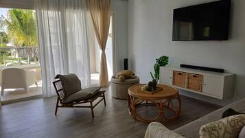Un salon moderne avec un canapé, un fauteuil, une table basse ronde et un téléviseur fixé au mur.