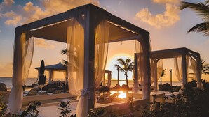 A beachside resort with overwater bungalows, lounge chairs, and a sunset view. - TRACADERO Beach Club and Holidays Rentals (San Rafael del Yuma)