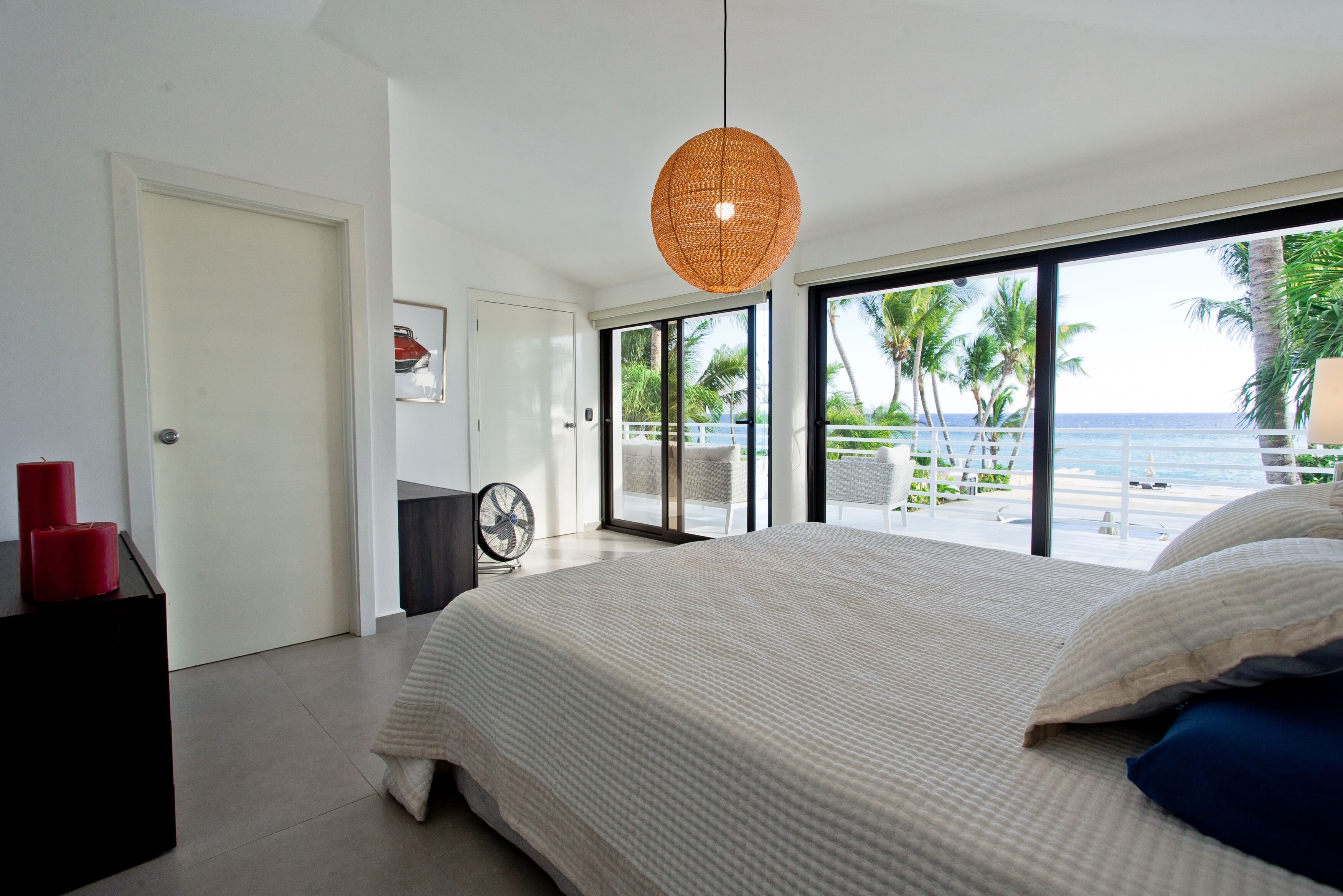 A bedroom with a large bed, a view of the beach, and a door leading to another room.