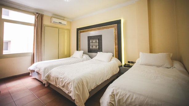 Habitación de hotel con dos camas individuales, un ventanal con cortinas, un equipo de aire acondicionado y un adorno en la pared.