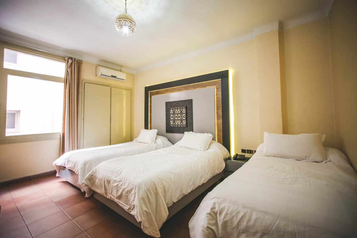 A hotel room with two single beds, a large window with curtains, an air conditioning unit, and a decorative wall piece.