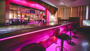 Una zona de bar con una barra de madera, taburetes y una variedad de botellas de licor.
