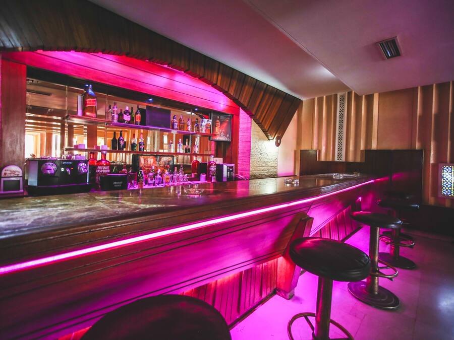 A bar area with a wooden counter, bar stools, and a variety of liquor bottles.