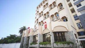 Un hotel de varios pisos con fachada color crema, varios balcones y banderas rojas.