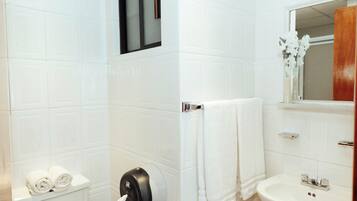 Baño con azulejos blancos, inodoro con toallas, secamanos, lavamanos y espejo.