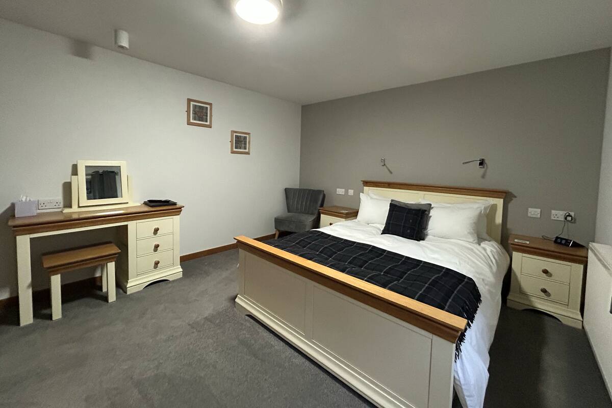 Quarto de hotel com cama, mesas de cabeceira, escrivaninha e uma cadeira.