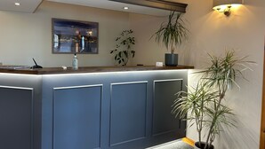 A reception desk with a modern design, a framed artwork above it, and a potted plant to the right. - Karrawa Guest House (Kirkwall)