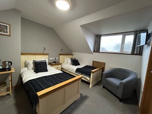 Ein Schlafzimmer mit zwei Betten, einem grauen Sessel, einem Fenster und einer Deckenleuchte.