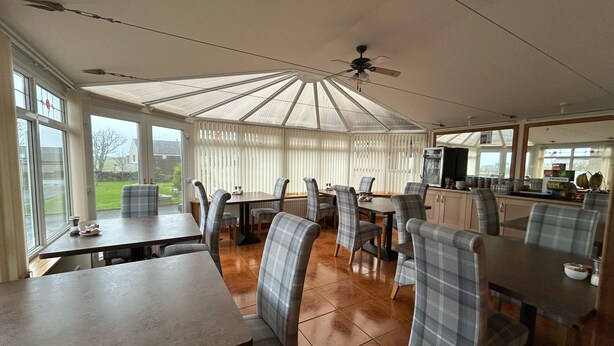 A spacious dining area with high ceilings and large windows, featuring plaid chairs and a central table. - Karrawa Guest House (Kirkwall)