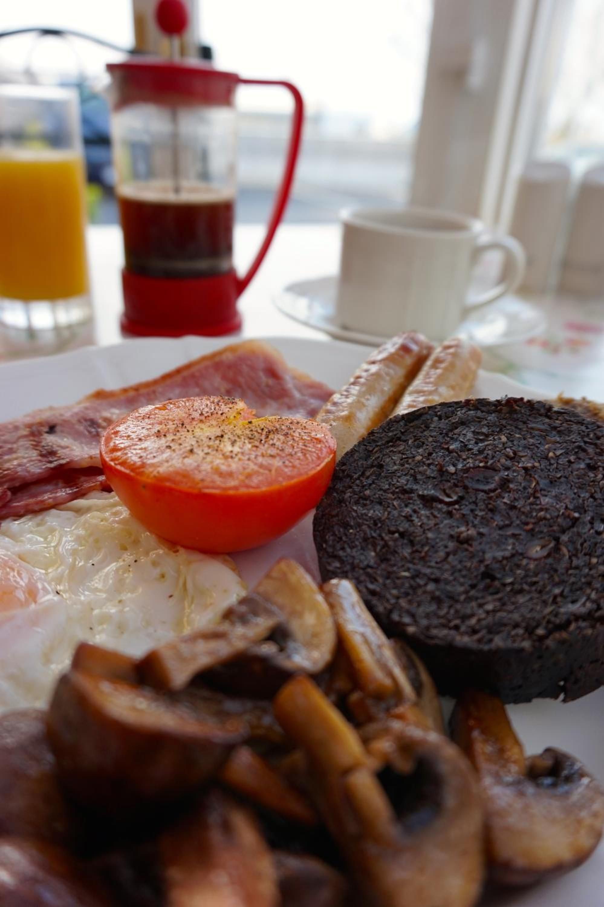 Ein Frühstücksteller mit Eiern, Speck, Pilzen, einer Tomate und einer Scheibe Blutwurst.