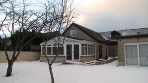 A house with a covered patio, a garage, and a snow-covered yard. - Karrawa Guest House (Kirkwall)
