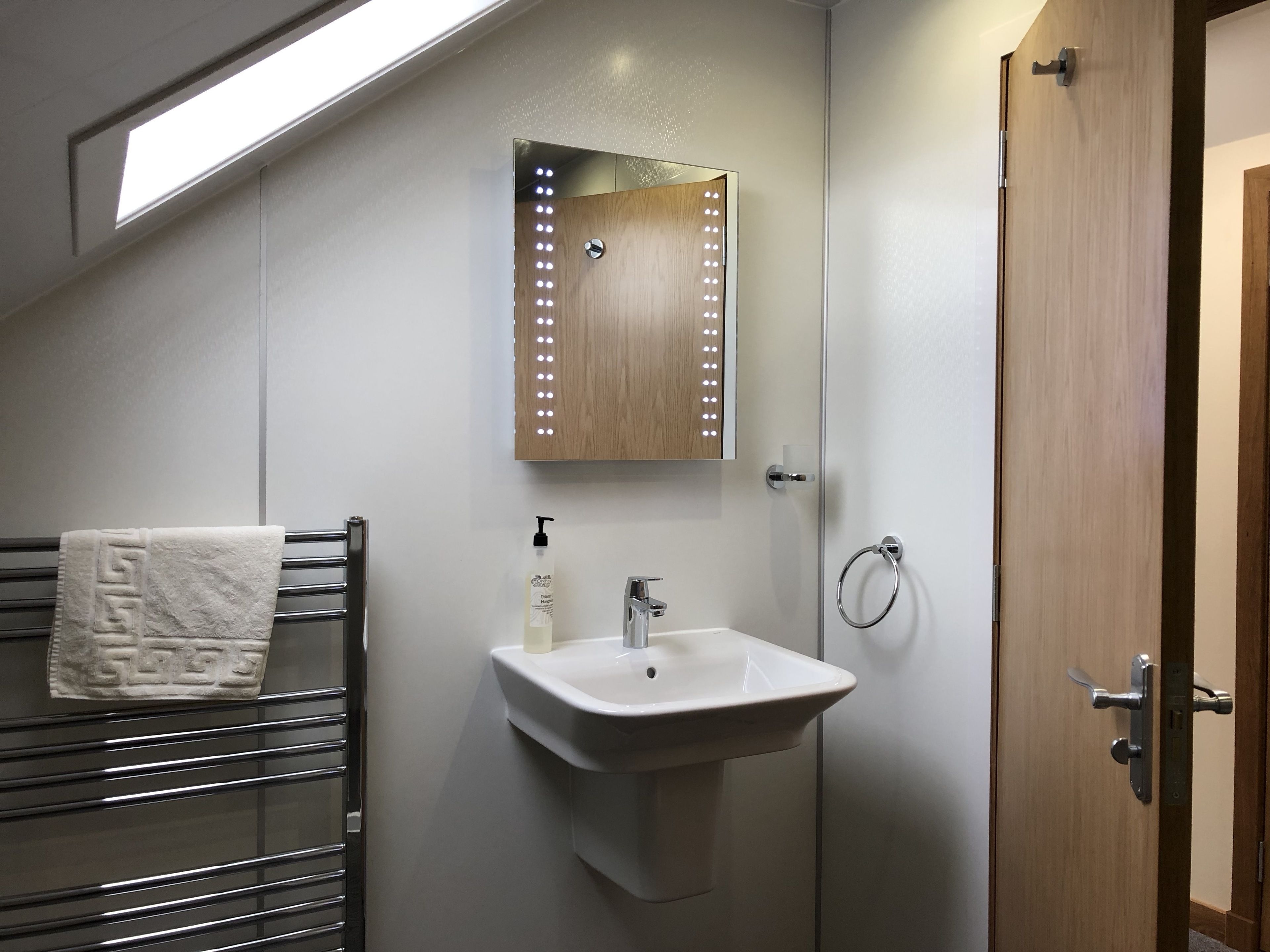 Une salle de bain avec un puits de lumière, un porte-serviettes, un lavabo avec un miroir et une porte en bois.