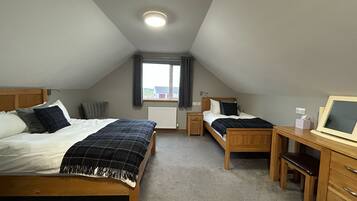 A bedroom with two beds, a desk, and a window.
