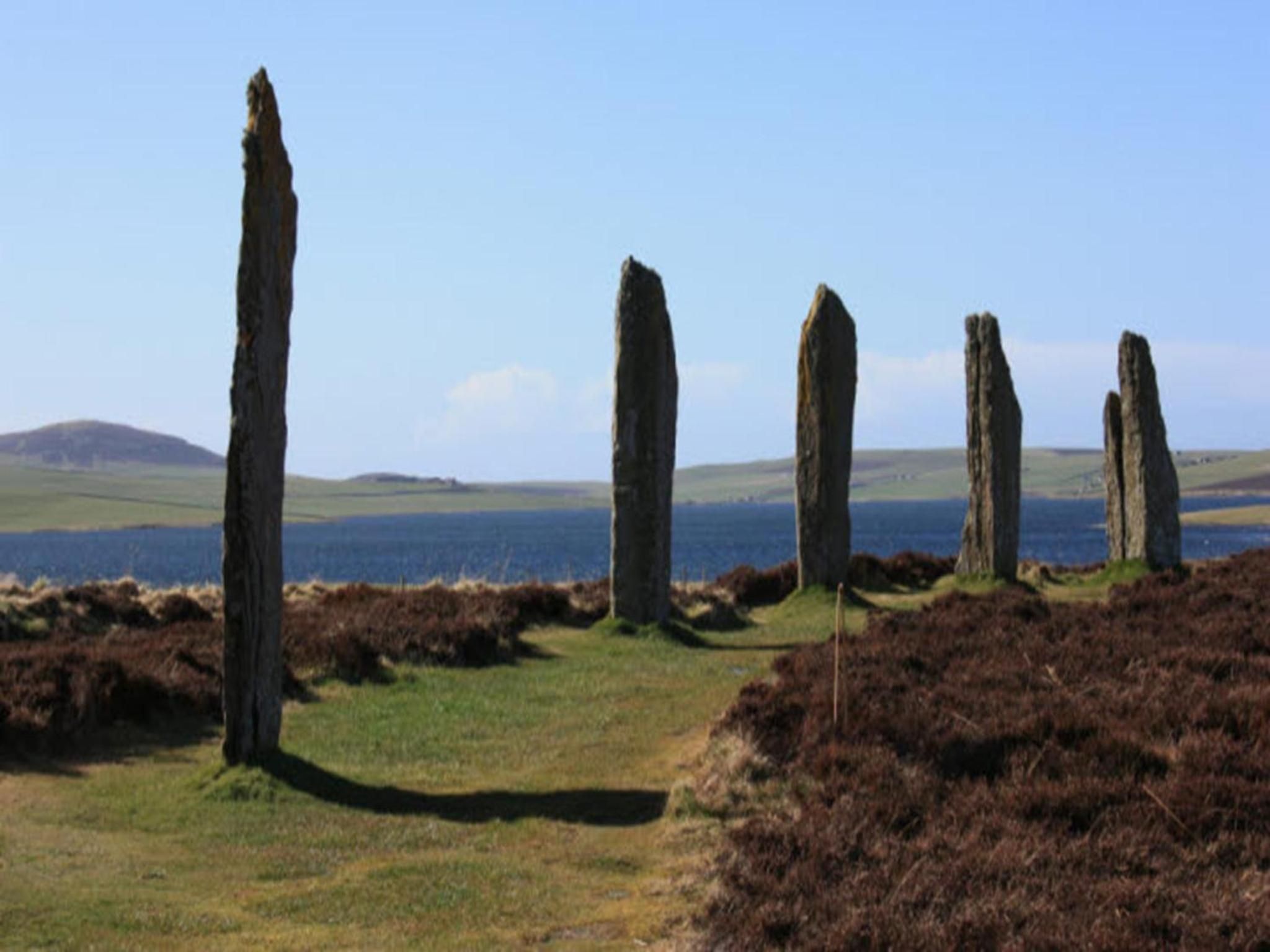A landscape with standing stones, grassy terrain, and a body of water in the background.