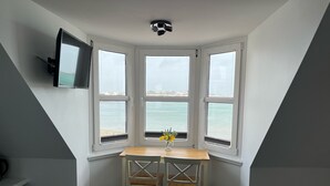 Une pièce d’angle avec une baie vitrée donnant sur un plan d’eau, une petite table avec des chaises et un téléviseur fixé au mur.