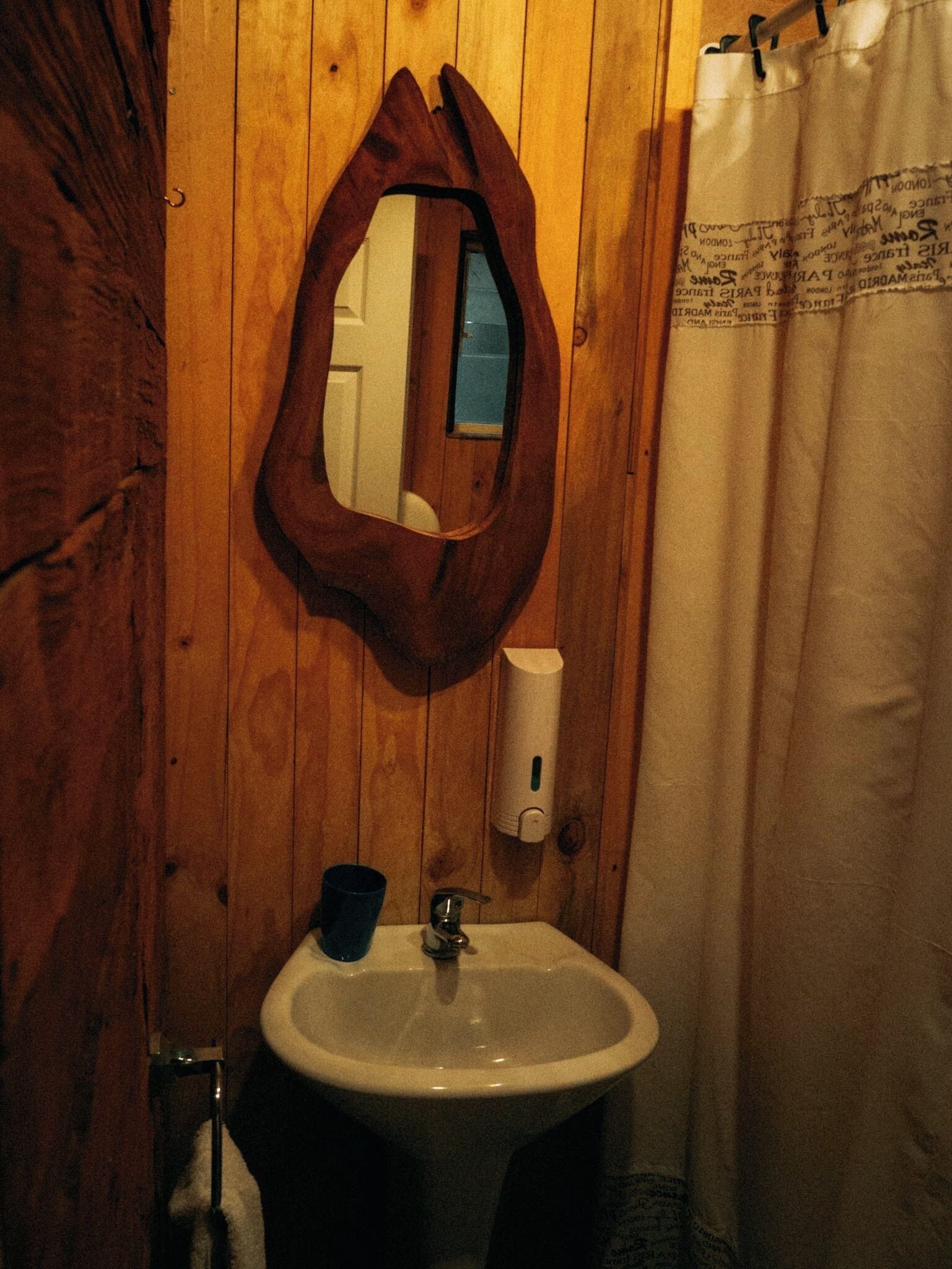 Un baño de madera con lavabo, espejo y cortina de ducha.