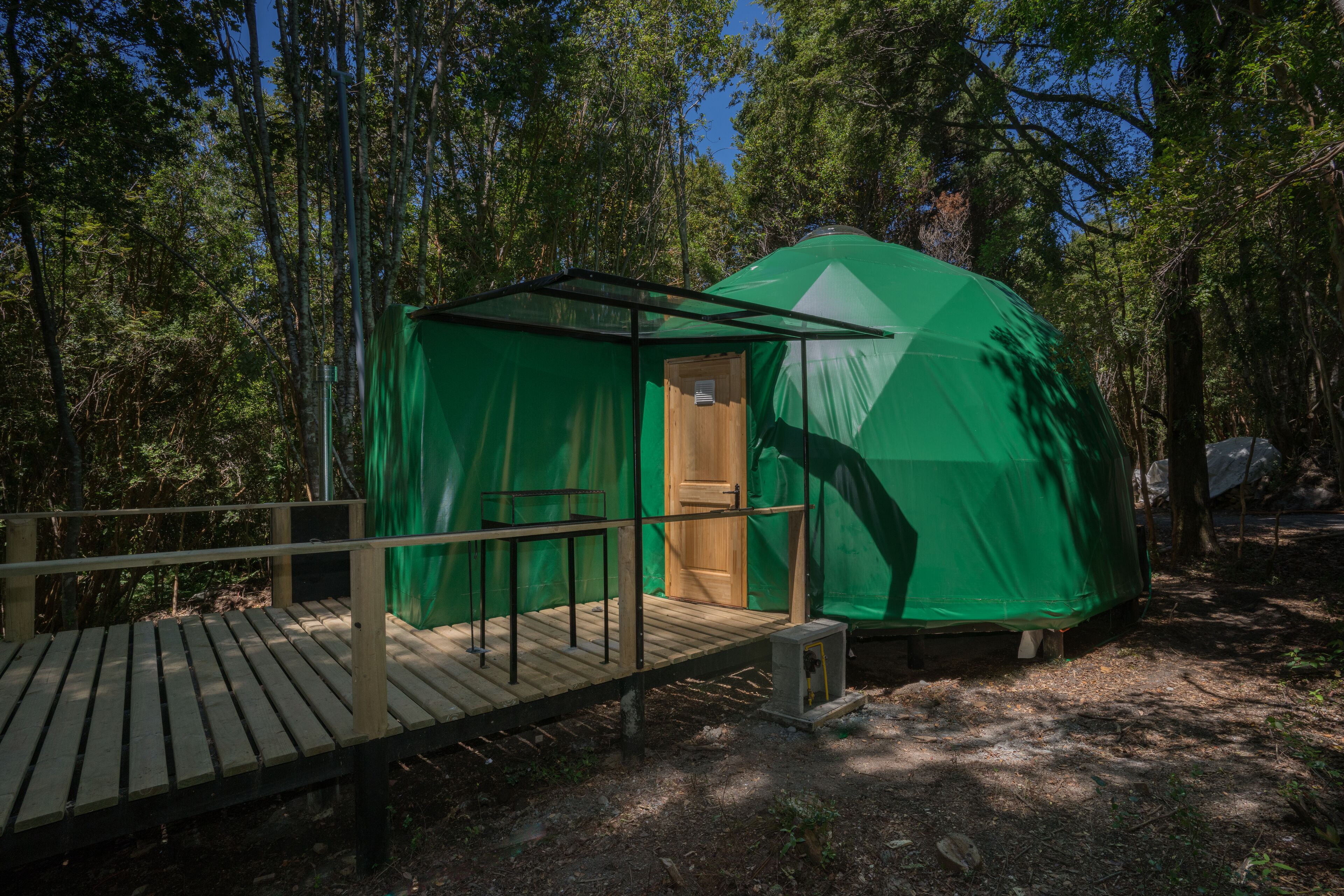 A green tent-like structure with a wooden deck in a forest.