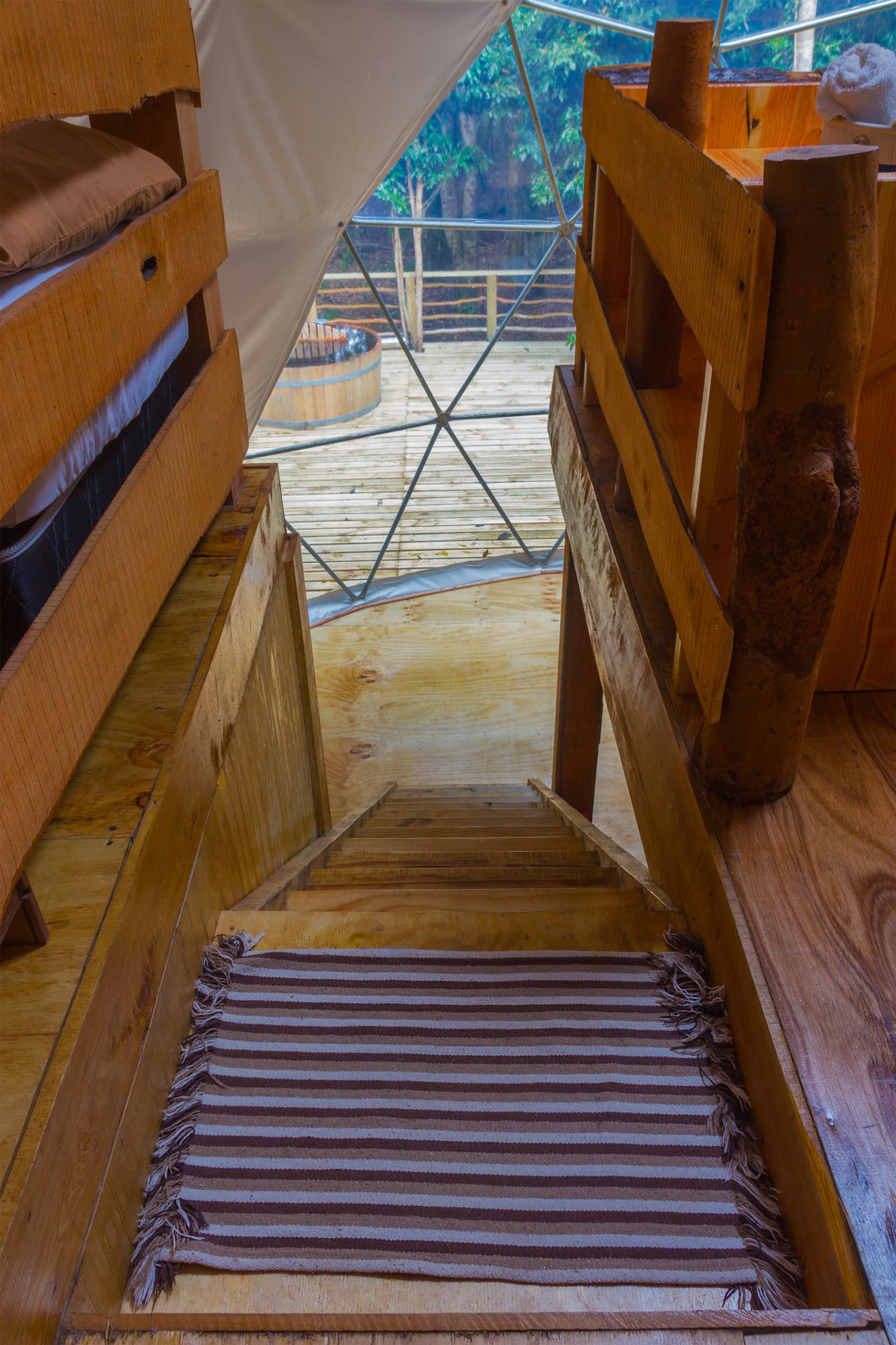 A wooden staircase leading to a wooden deck with a view of greenery outside.