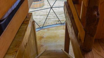 A wooden staircase leading to a wooden deck with a view of greenery outside.
