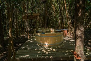Un jacuzzi de madera rodeado de árboles sobre una terraza de madera.