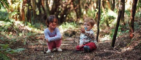 Two children sitting on a forest floor surrounded by trees.