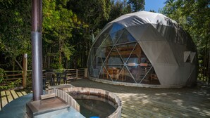Una estructura de domo geodésico con terraza de madera y bañera de hidromasaje.