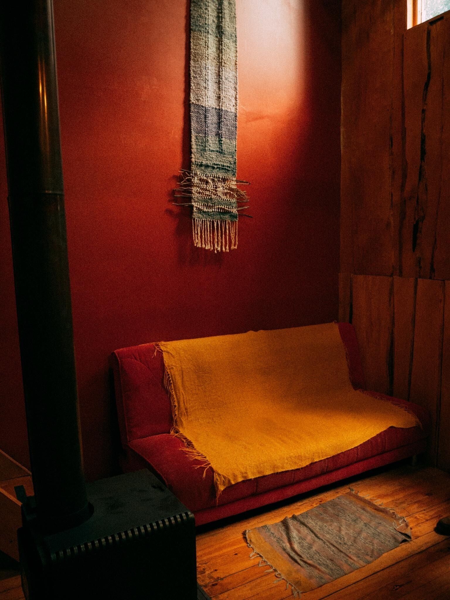 Una habitación acogedora con un sofá rojo, una alfombra pequeña y un tapiz en la pared.