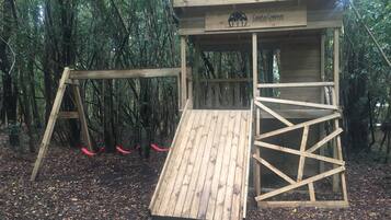 A wooden play structure in a forested area with a sign reading "Cabañas Ensenada SOSQUE NATIVE."