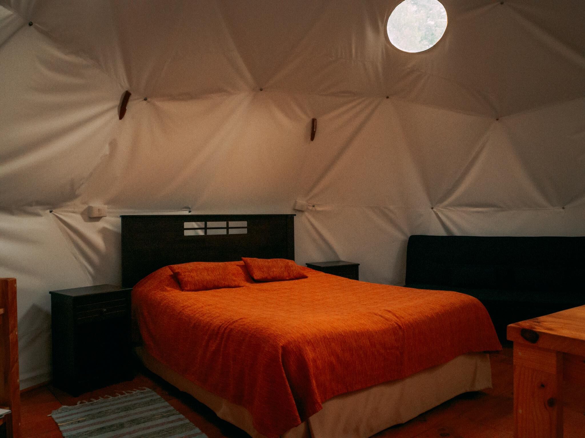 Una habitación tipo tienda con una cama, dos mesitas de noche y un banco de madera.