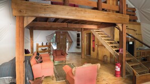 Una habitación amplia con techo de madera, una escalera y una cama con manta azul y blanca a rayas.