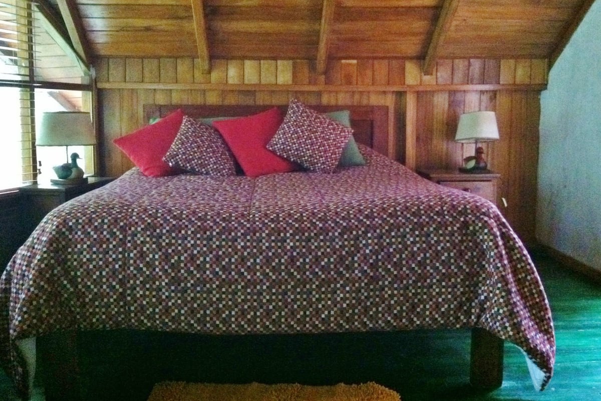A wooden-paneled room with a bed featuring a patterned bedspread and multiple pillows.