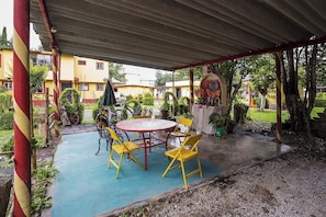 An outdoor patio with a round table and yellow chairs, surrounded by greenery and a covered area. - Capital O Hotel Meson Del Rio, Tepotzotlan (Tepotzotlán)
