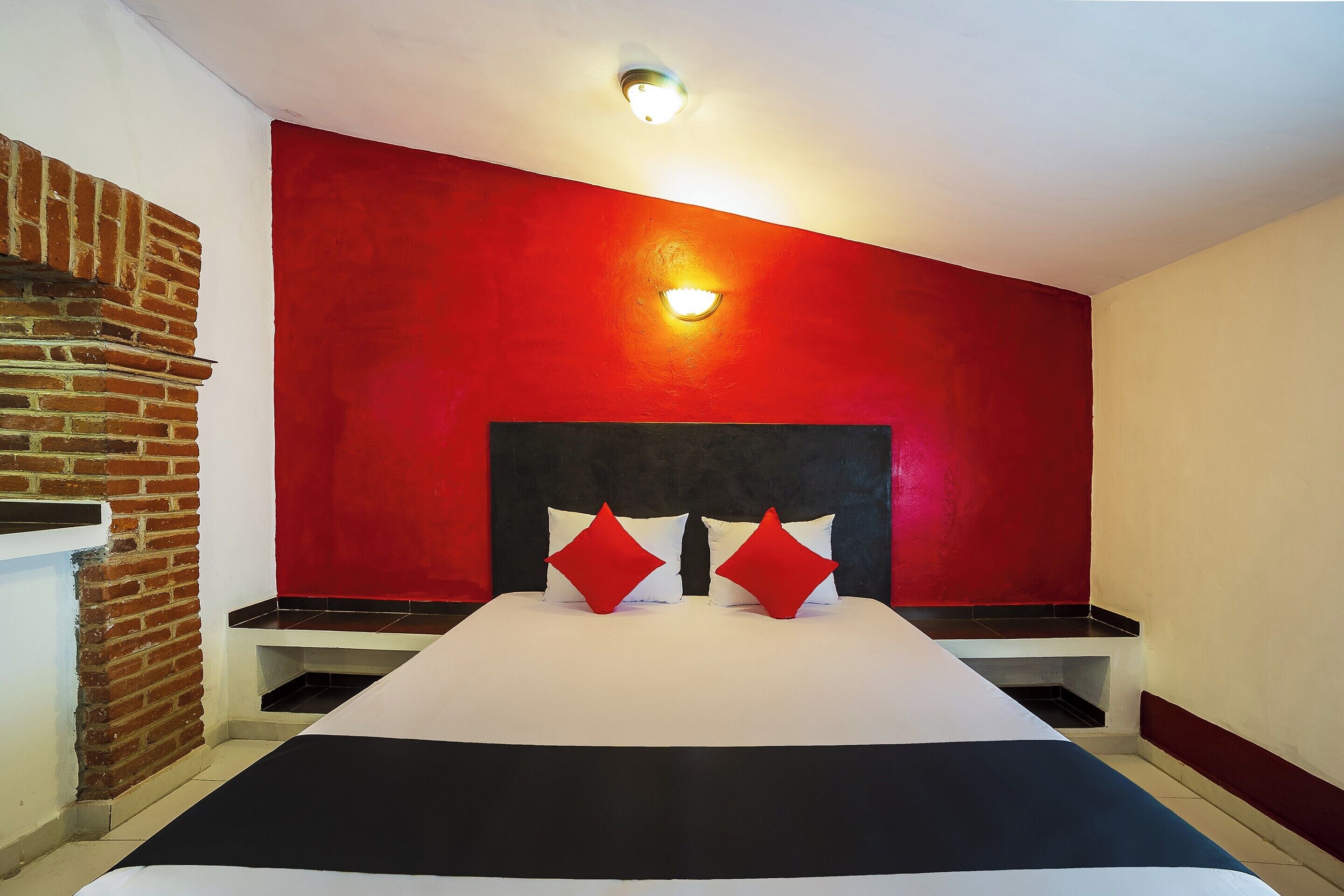 A hotel room with a brick wall, a red accent wall, a black headboard, a white bedspread, and two red pillows.